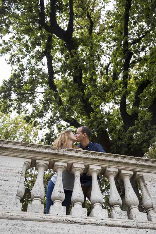 Kissing underneath tree terrace overlook with green leaves and ancient roman columns as photo props