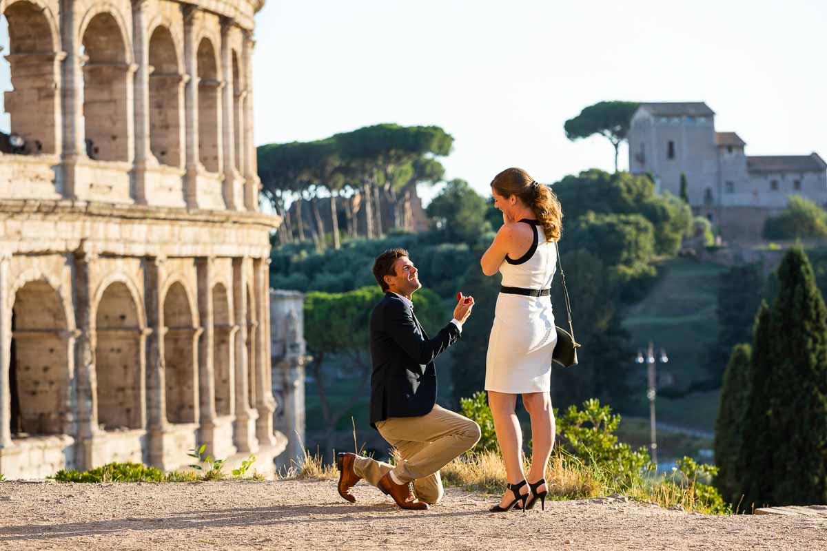 Man kneeling down for a Colosseum proposal in Rome candidly photographed at a distance by a professional photographer.