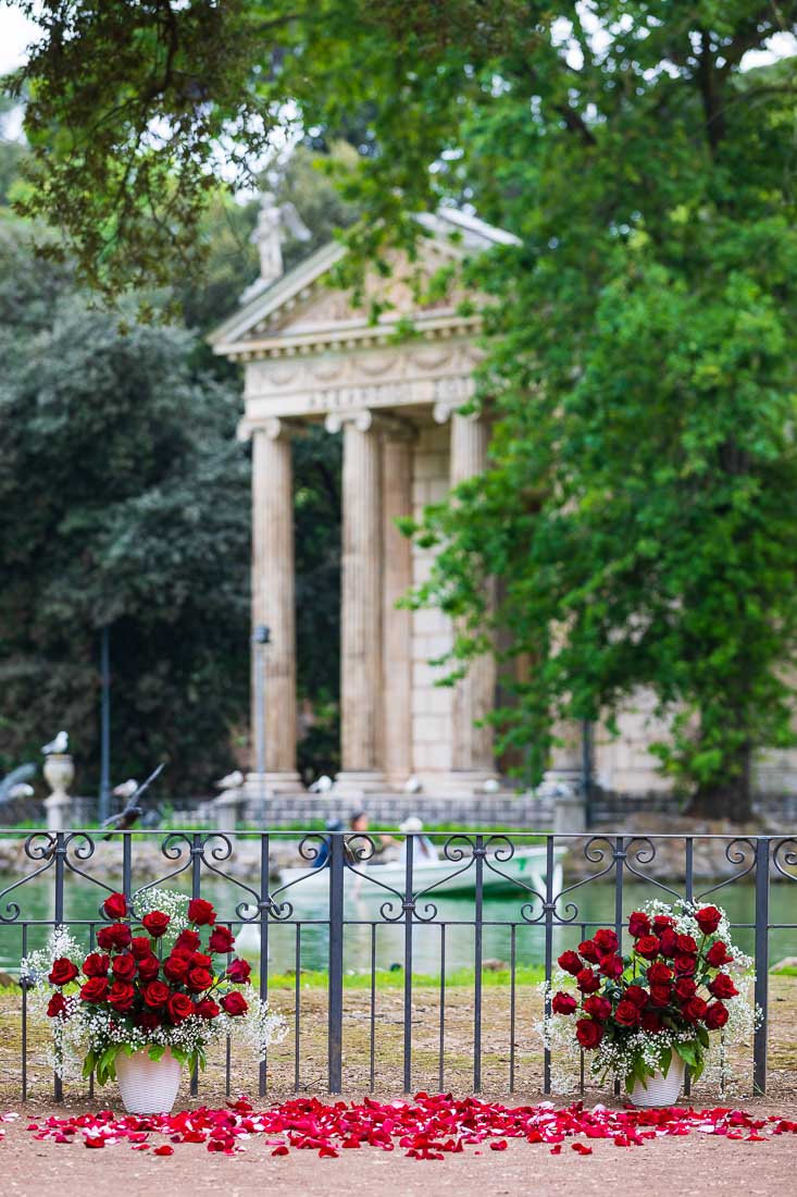A small angle Villa Borghese lake set up by the lake for a romantic wedding marriage engagement using 2 vases of red roses together with rose petals on the ground