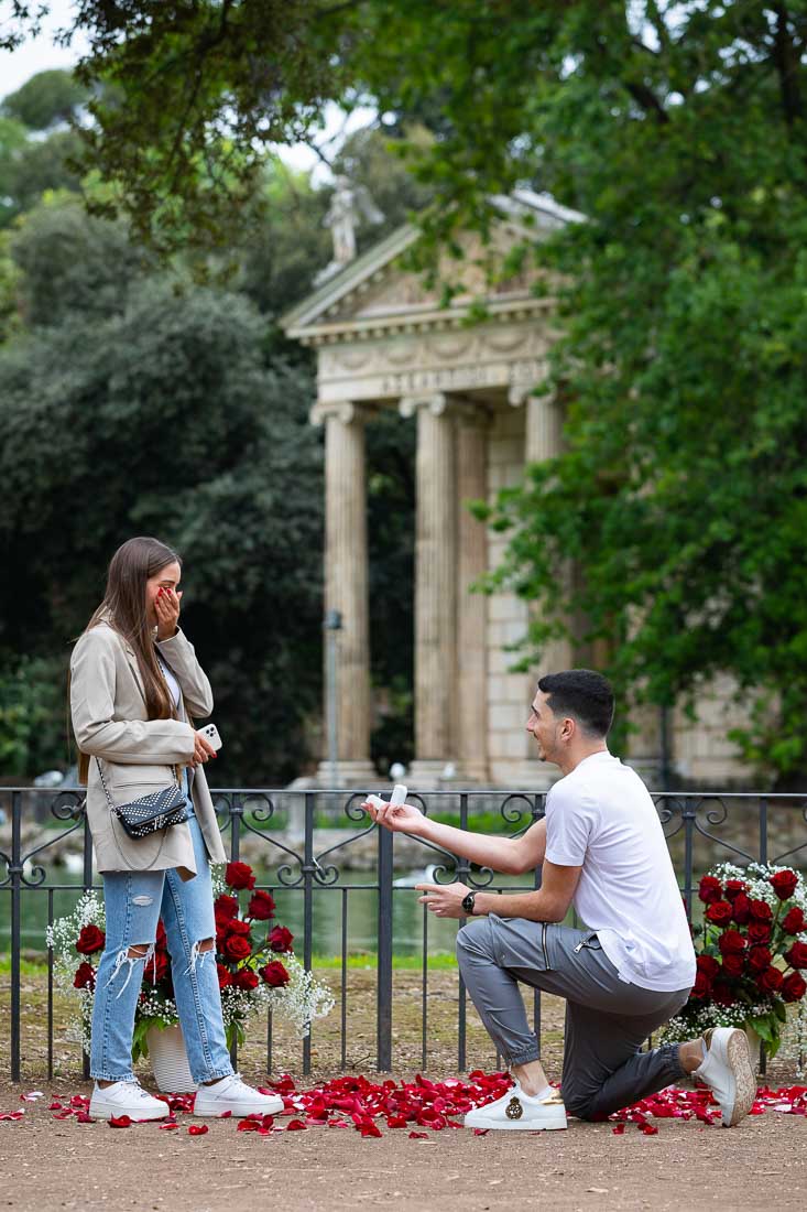 Romantic Rome Proposal. Knee down Surprise Wedding Engagement at the Villa Borghese lake among beautiful red roses 