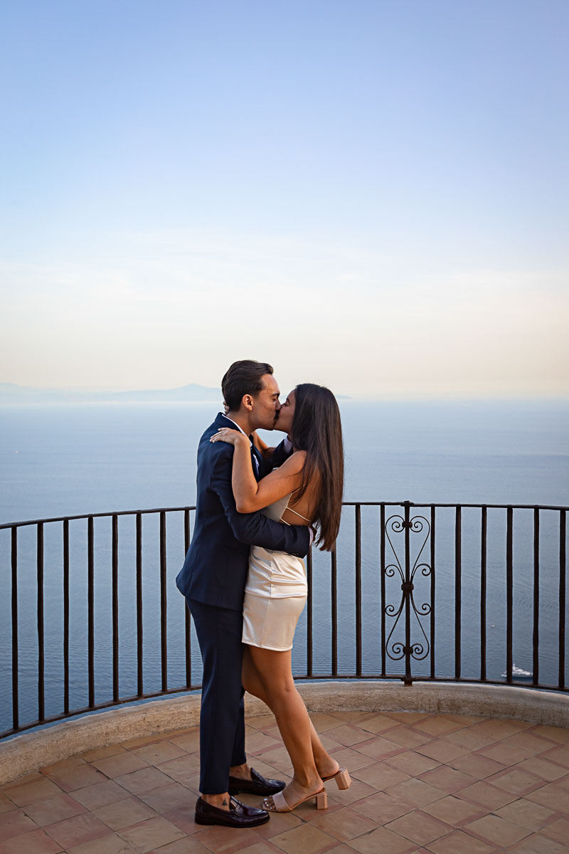 Couple kissing on a terrace overlooking the sea at sundown with horizon in background