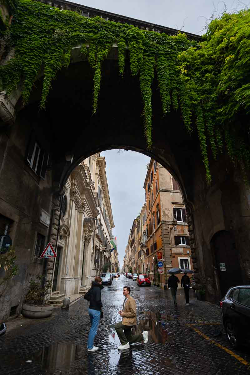 Proposing under Arco Farnese across Via Giulia on a rainy day in Rome