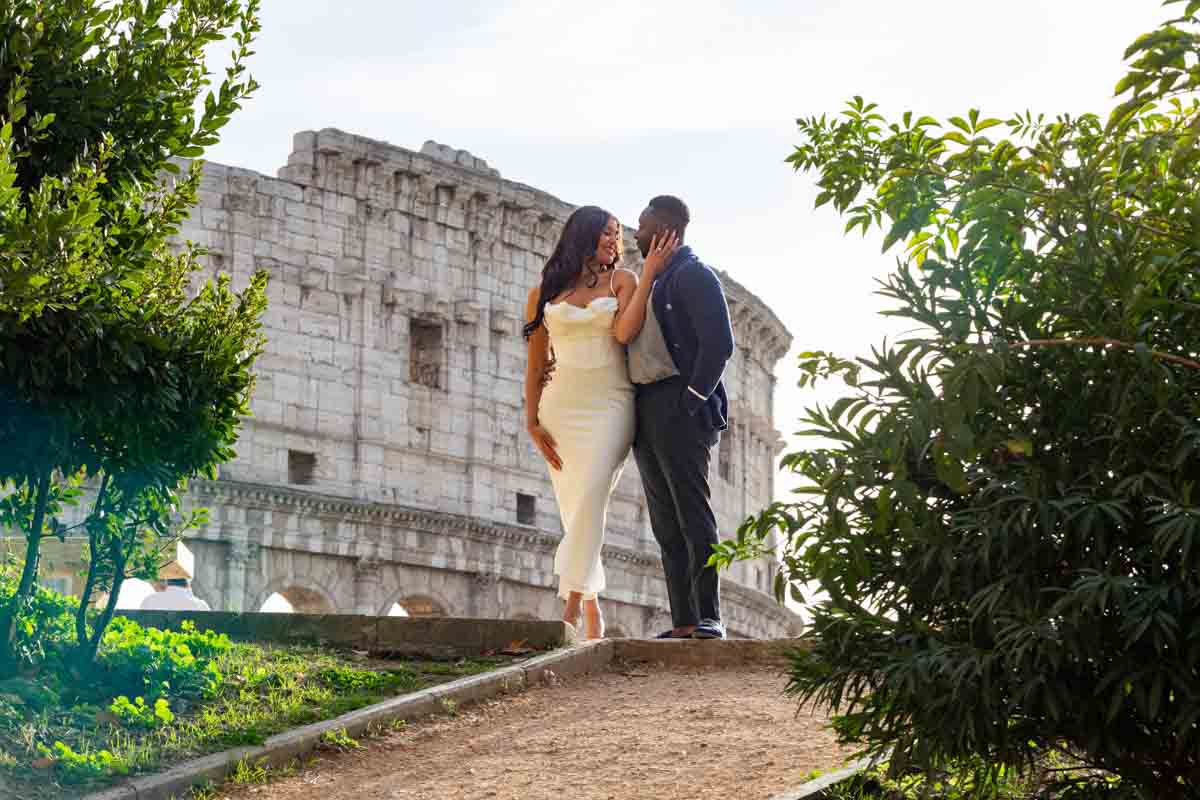 Couple standing before the ancient roman colosseum monument while taking unique and creative photographs of the their engagement