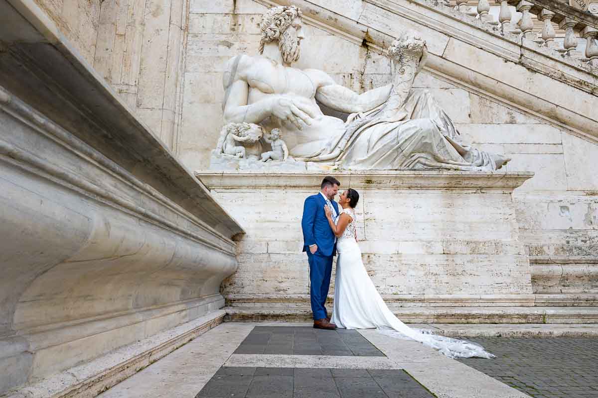 Wed photos in Roma with the bride & groom standing beneath an ancient roman marble statue 