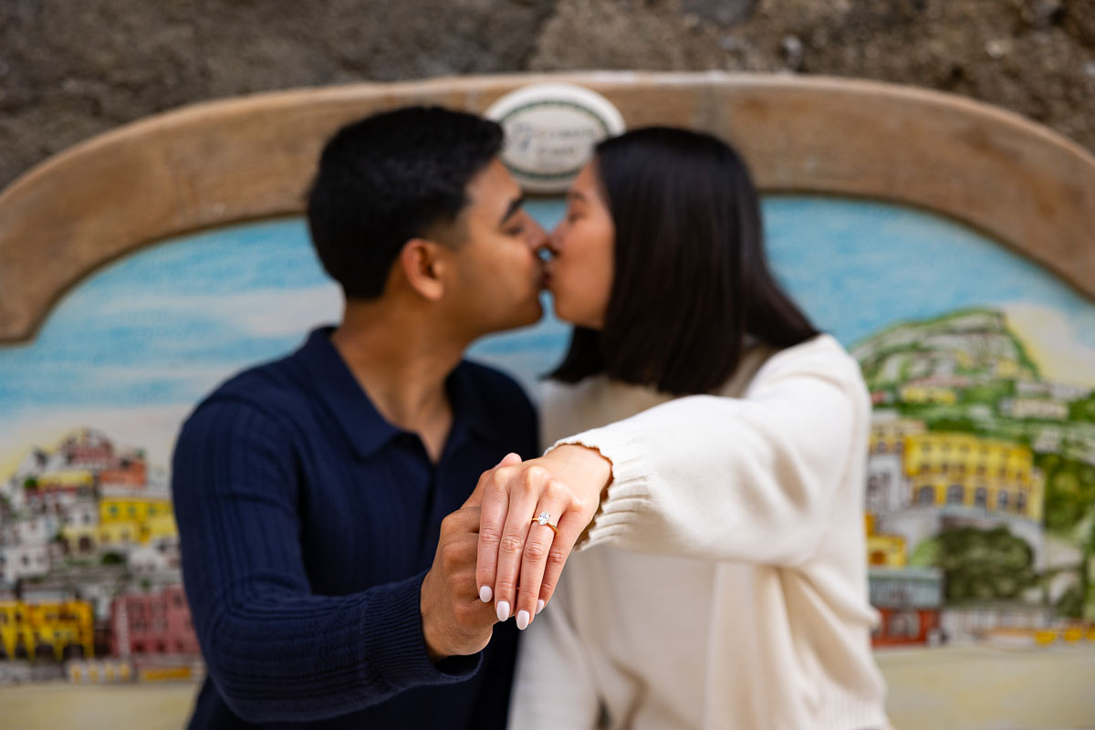 Kissing with the engagement ring shown forefront and the couple kissing the background