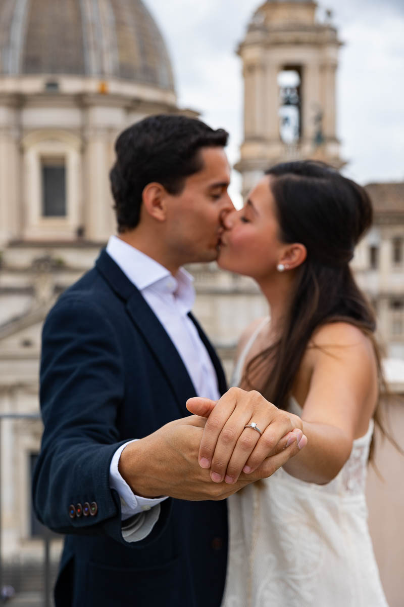 Closeup of the engagement ring with the couple kissing in the background