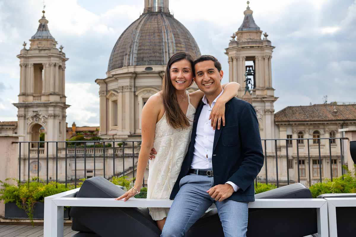 Sitting down portrait of a couple posing in front of the camera after a Terrace proposal in Rome with a view over church domes