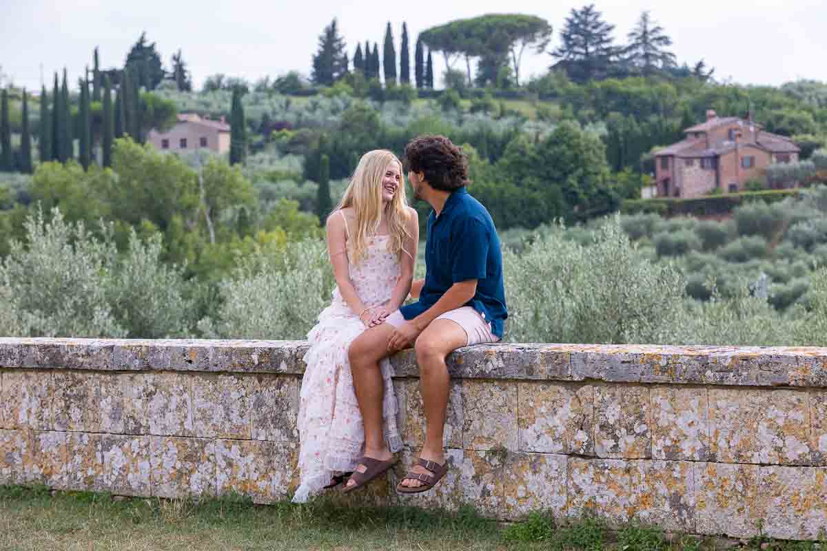 Couple sitting down on a ledge before the country background in Italy