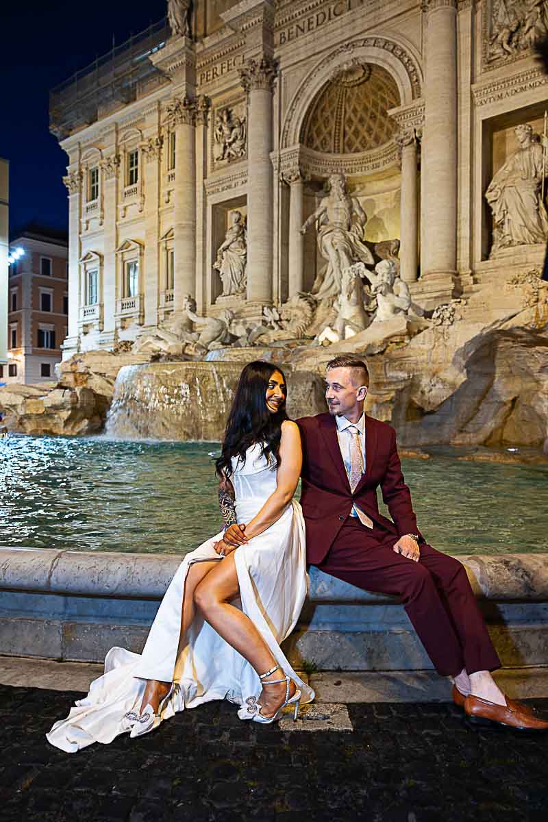Sitting down at the Trevi fountain during a photographer session taking unique and creative photos in wedding attive in one of Rome's most beautiful and romantic location 