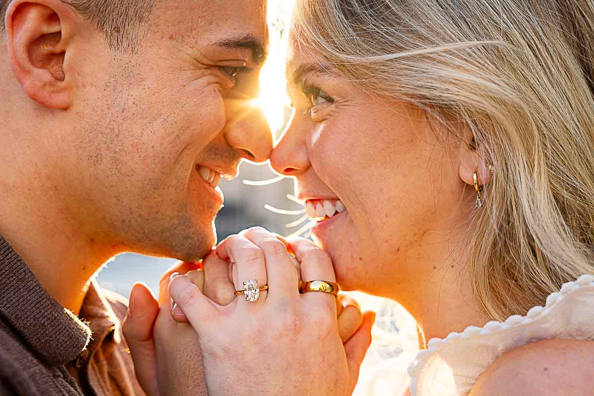 Close up sideways portrait of a couple at sun rising in the background with the engagement ring 