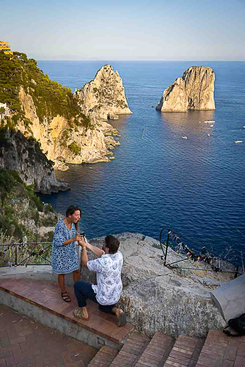 Kneel down surprise wedding marriage Capri engagement proposal on the Augustus Gardens with a stunning view of the faraglioni rocks in the far distance 
