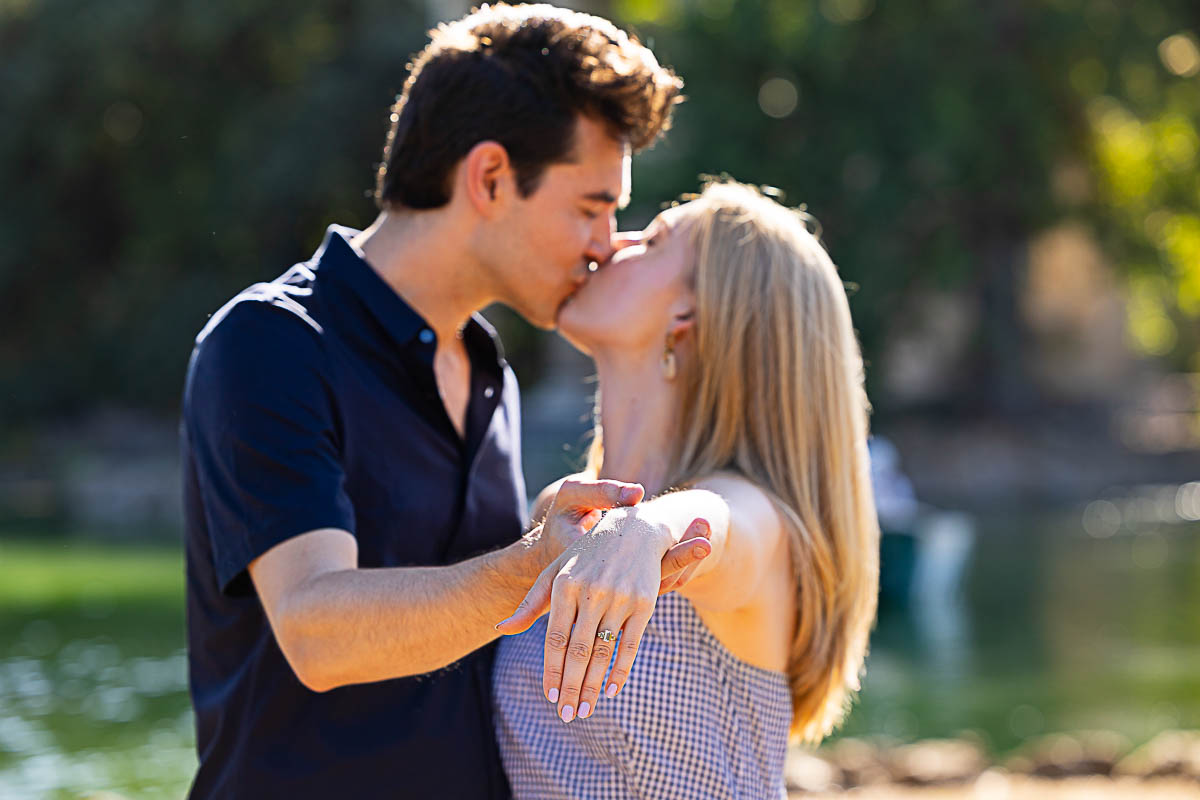 A kiss blurred in the background with the engagement ring in the forefront in focus