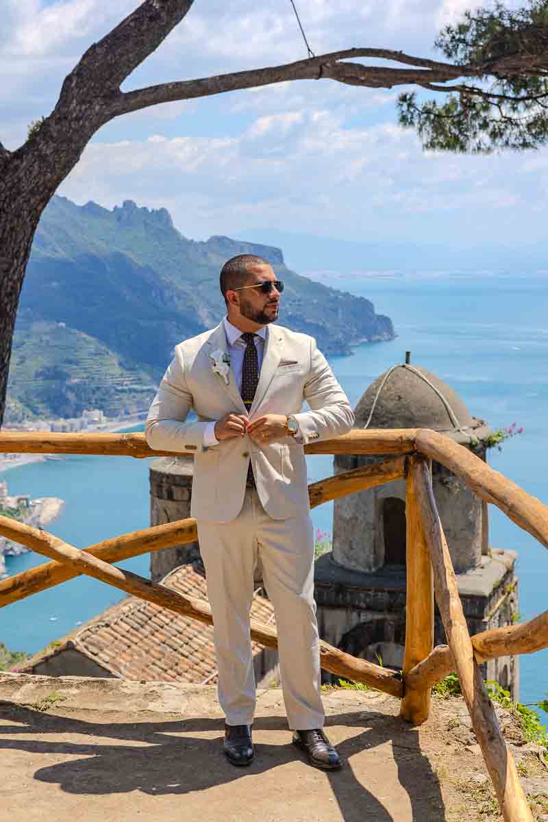 Solo groom picture shot portrait while adjusting the jacket in one beautiful panoramic spot overlooking ancient church dome and the coast of Amalfi 