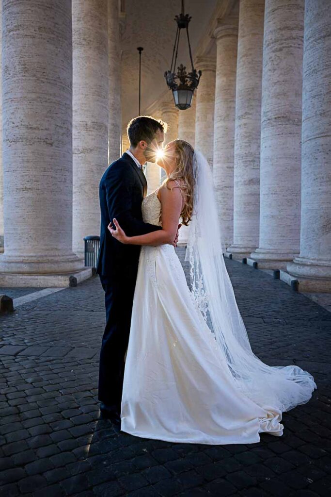 Sideways picture of bride & groom during a photographer session while kissing with the sun rays in between