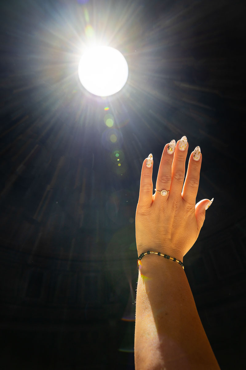 Newly engaged couple showing a diamond ring raised towards the sunlight entering through the dome opening during a romantic portrait session
