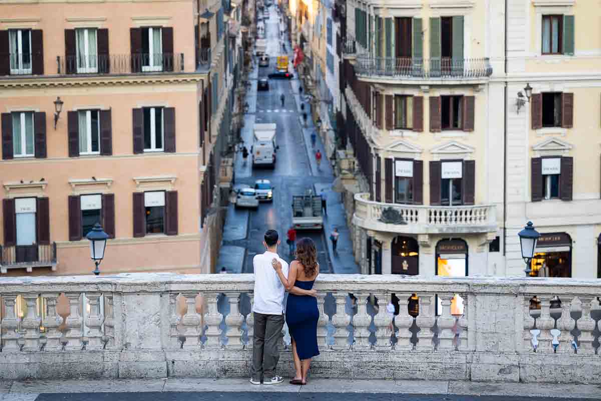 Newly engaged couple standing together overlooking Via Condotti, captured in a refined editorial portrait from the top of the historic staircase, creating a timeless visual keepsake of their special day.
