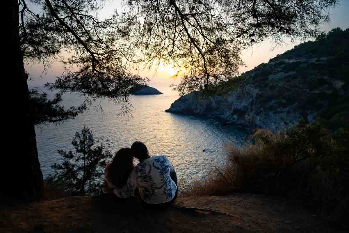 Panoramic sunset portrait of two women sitting side by side overlooking the sea and coast, celebrating their engagement with sweeping views across the Monte Argentario coastline. 