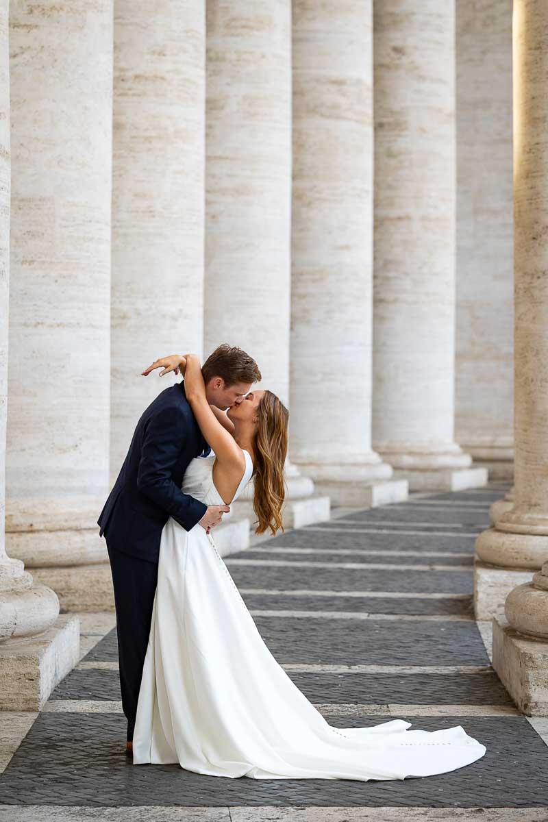 Intimate kiss beneath the white marble colonnade, captured as a romantic image with the sweeping rows of classical pillars forming a geometric frame
