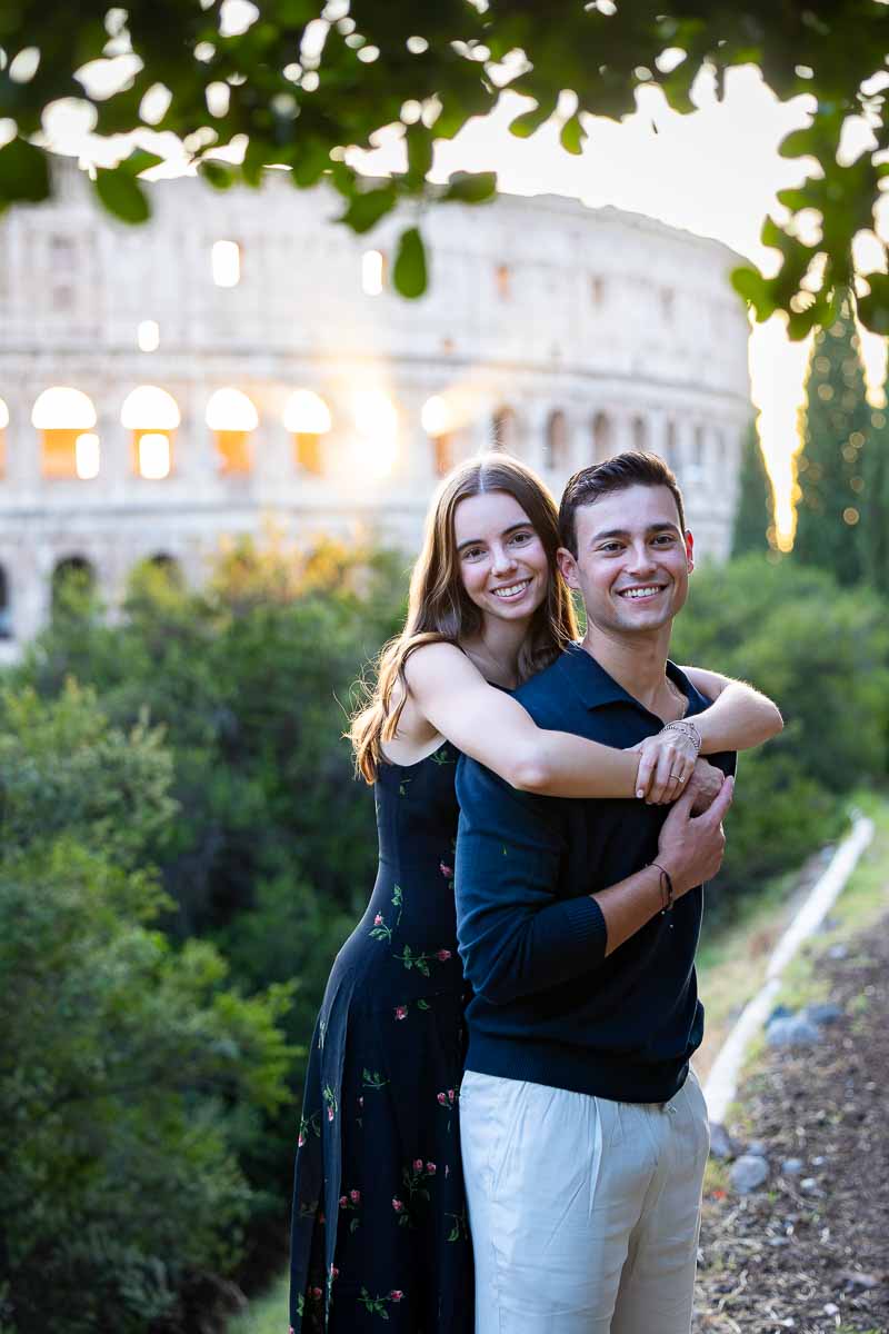 Embracing pose for engaged portrait in a park with a view of the Colosseum behind them 